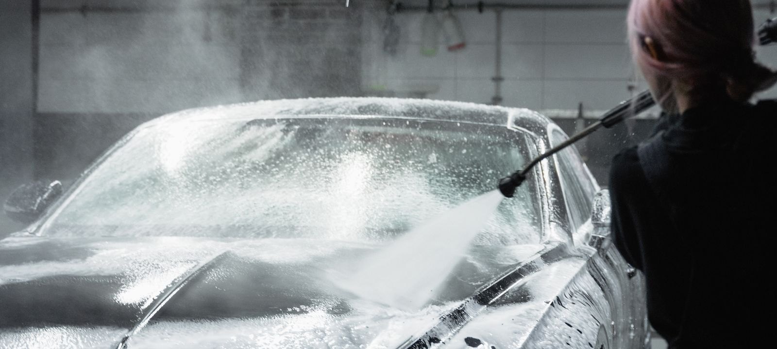 A car being pressure-washed with foam in a wash bay